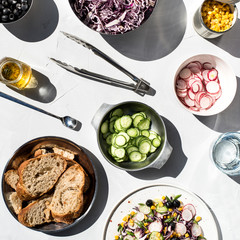 Photo of a fresh spring salad on a white porcelain plate and vegetable mix of ingredients in metal bowl on a white rustic background sunlight with shadows
