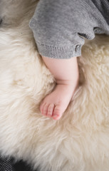 A beautiful soft delicate warm young baby foot photographed with a shallow depth of field. gentle calm colours and feel. baby care and well being. babies feet on a cream fur rug.