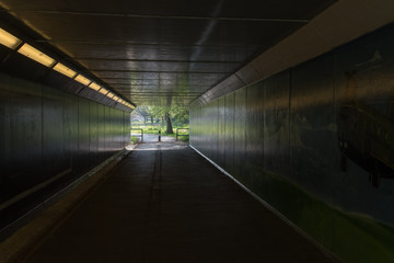 Tunnel walkway to park for pedestrians with lights on inside
