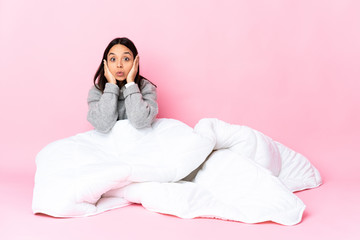 Young mixed race woman wearing pijama sitting on the floor frustrated and covering ears
