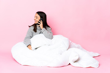 Young mixed race woman wearing pijama sitting on the floor keeping a conversation with the mobile phone with someone