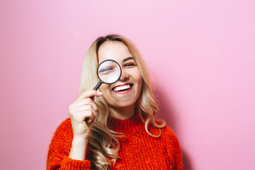 Portrait of a beautiful pretty blonde girl looking through magnifying glass isolated over pink background