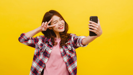 Smiling adorable Asian female making selfie photo on smartphone with positive expression in casual...