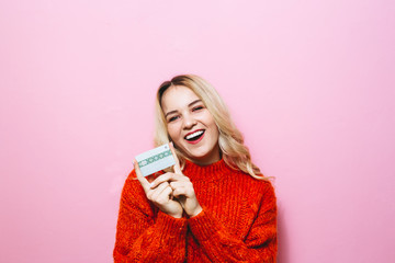 Portrait of a blond girl holding a credit card and smiling in the room on a pink background