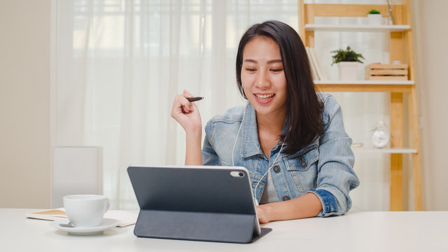 Freelance Business Women Casual Wear Using Tablet Working Call Video Conference With Customer In Workplace In Living Room At Home. Happy Young Asian Girl Relax Sitting On Desk Do Job In Internet.