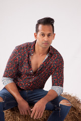 Fototapeta premium Handsome man thoughtfully sitting on a bale of hay