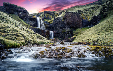 Typical Icelandic scenery. Fresh green hills and waterfall.  Picture of wild area. Iceland. Amazing nature landscape with colorful sky during sunset.
