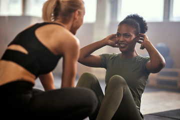 Smiling woman doing sit-ups in a gym with a friend - obrazy, fototapety, plakaty