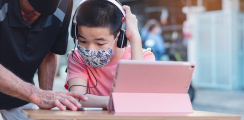 Happy asian disabled on wheelchair wearing Handmade mask to protection flu Covid 19 or Coronavirus, Stay at home to prevent the spread of the virus disease 2020, Boy uses his tablet to study online.