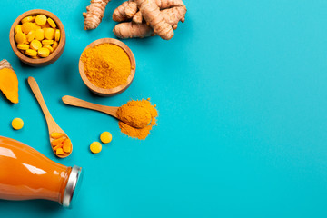 Fototapeta na wymiar Mess of turmeric plant in different conditions: fresh, dry root, pills, powder and cut plant on blue background. Flat lay style. Place for text.