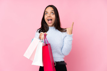 Young woman with shopping bag over isolated pink background pointing up and surprised