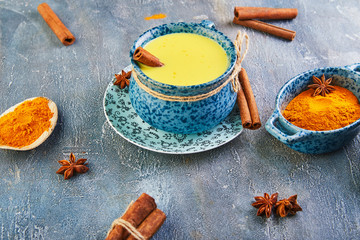 Obraz na płótnie Canvas Golden milk with turmeric, cinnamon sticks, turmeric and anise on a gray cement background. Turmeric detox tea and ingredients. copy space