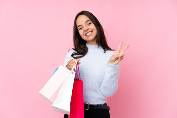 Young woman with shopping bag over isolated pink background smiling and showing victory sign