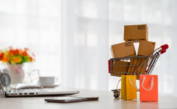 Online shopping concepts - Product package boxes in cart and shopping bag with laptop, smart phone and credit card on desk with copy space