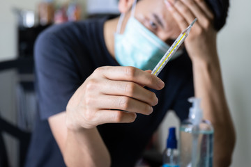 Asian man hand holding thermometer after check boby temperature during coronavirus home quarantine (select focus)