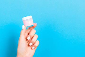 A jar of cosmetic product in a female hand at blue background with copy space