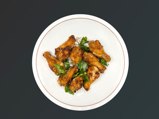 Crispy fried chicken, fragrant, herbs served on a round white plate. Isolated on black background.