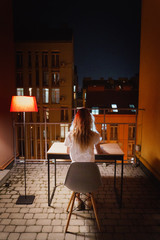Young girl at night using a laptop on the terrace against the background of colored houses