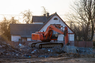 Fototapeta na wymiar Excavator demolishes an old wooden house in the village for new construction project. Tearing Down a Houses. Building removal made of bricks. Hard equipment for demolition works