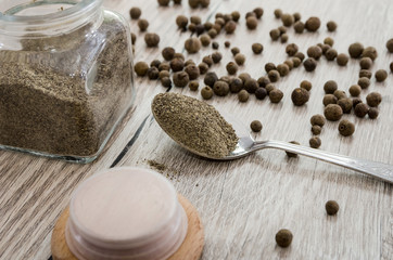 ground black pepper in a spoon and pepper peas on a wooden background. Close-up.
