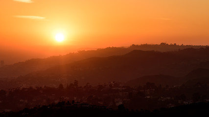 Fototapeta premium Sunset over the Hollywood Hills, Los Angeles. The sky is various shades of orange and yellow.