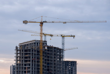 Tower cranes working at construction site against blue sky. Crane lifting a concrete bucket. Construction process of the new residential buildings. Transportation blocks and pouring of the cement mix