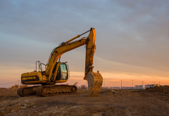 Excavator on earthworks at construction site on sunset background. Backhoe digs ground for the foundation and for paving out sewer line. Construction machinery for excavating