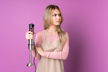 Teenager Russian girl using hand blender isolated on purple background portrait