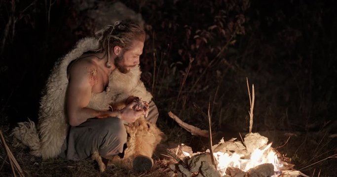 Man in sheepskin eating at a campfire at night