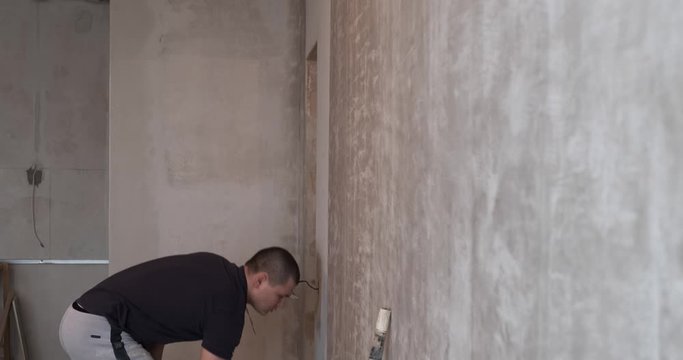 Male builder is working at construction site, painter is applying with roller white product to protect surface from moisture and fungi, painter at work, station wagon builder, repair in apartment