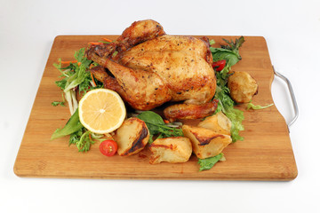 Whole roasted grilled chicken poultry bird with baked potato vegetable salad tomato lemon on wooden cutting board white background