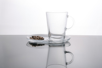 Empty glass coffee cup and roasted coffee beans. White background, dark surface.