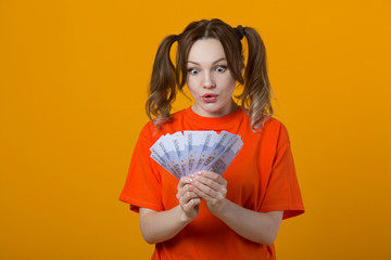beautiful young woman in a t-shirt on a yellow background with euro in hands