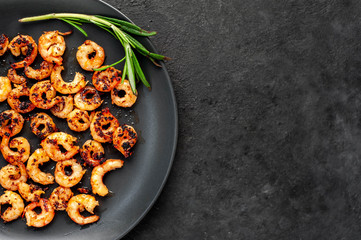 grilled prawns on a black plate with lemon and rosemary on a stone background with copy space for your text
