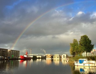 Naklejka na ściany i meble rainbow over cloudy sky above harbour with light house boat