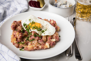 Norddeutscher Hamburger Labskaus mit Rindfleisch Corned Beef, Rote Beete, Kartoffeln, Saure Gurken, Spiegelei, Rollmops und Bier auf Marmor