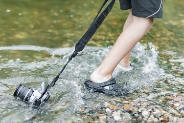 A boy stands in the river on outdooor and destroys a mirrorless photo camera. The concept of...