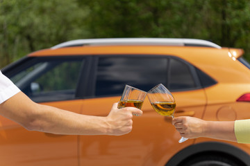 A couple celebrates buying a new car. Hands a man and a woman clink glasses against the background of the vehicle