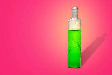 glass bottle with green refreshing herbal drink in pink background