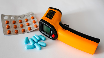 Remote electronic thermometer on a white background next to pills.