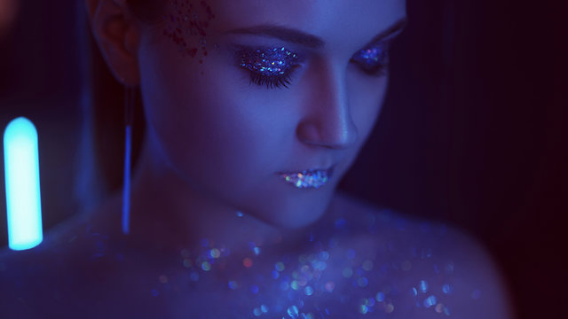 Neon girl portrait. Glitter makeup art. Woman with sparkling lips closed eyes in blue light.