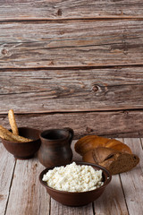 Fresh cottage cheese in a wooden bowl with a spoon, jar of sour cream on a wooden old background. Rich in Protein and Calcium healthy dairy product, low fat soft white cheese. With bread and hay.