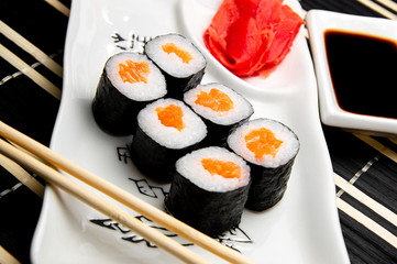 rolls with red fish on a white plate. Chinese chopsticks. Soy sauce in a white cup.