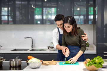 Young couples are helping to chop vegetables in the kitchen. Asian couple cooking together at the kitchen.
