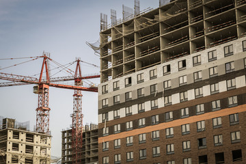 Several red cranes have been put to work on the construction of a modern multi-storey residential complex. Concept work for builder. Dream job. Large construction site.