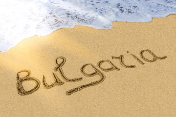 Bulgaria title on the light sand beach near the black sea coast. Brilliant sun ray falls on the letters. Hot season. Surf.