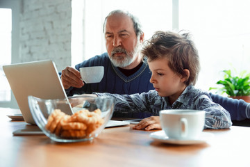 Using devices. Grandfather and his grandson spending time together insulated at home. Having fun, stadying online, reading and cleaning up. Concept of quarantine, family, love, realtions, togetherness
