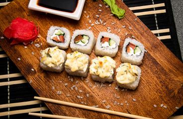 rolls with vegetables and curd cheese on a wooden board. Chinese chopsticks. Soy sauce in a white cup.