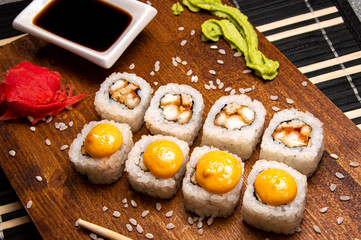 Orange rolls with chicken on a wooden board. Chinese chopsticks. Soy sauce in a white cup.