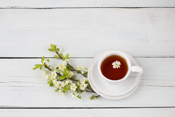 tea in a cup and cherry branches on the table